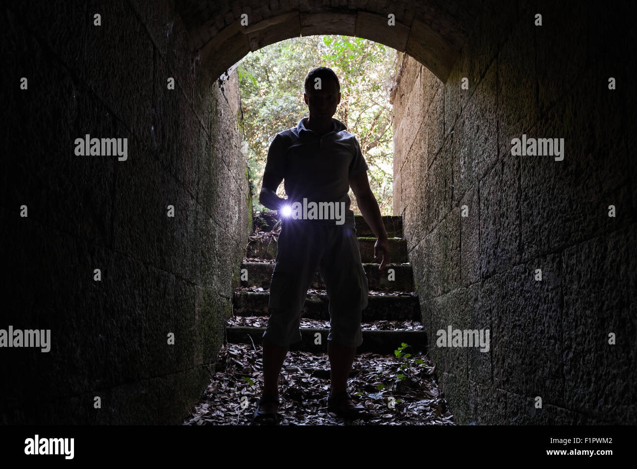 Giovane con una torcia elettrica entra nel tunnel di pietra e guarda al buio Foto Stock
