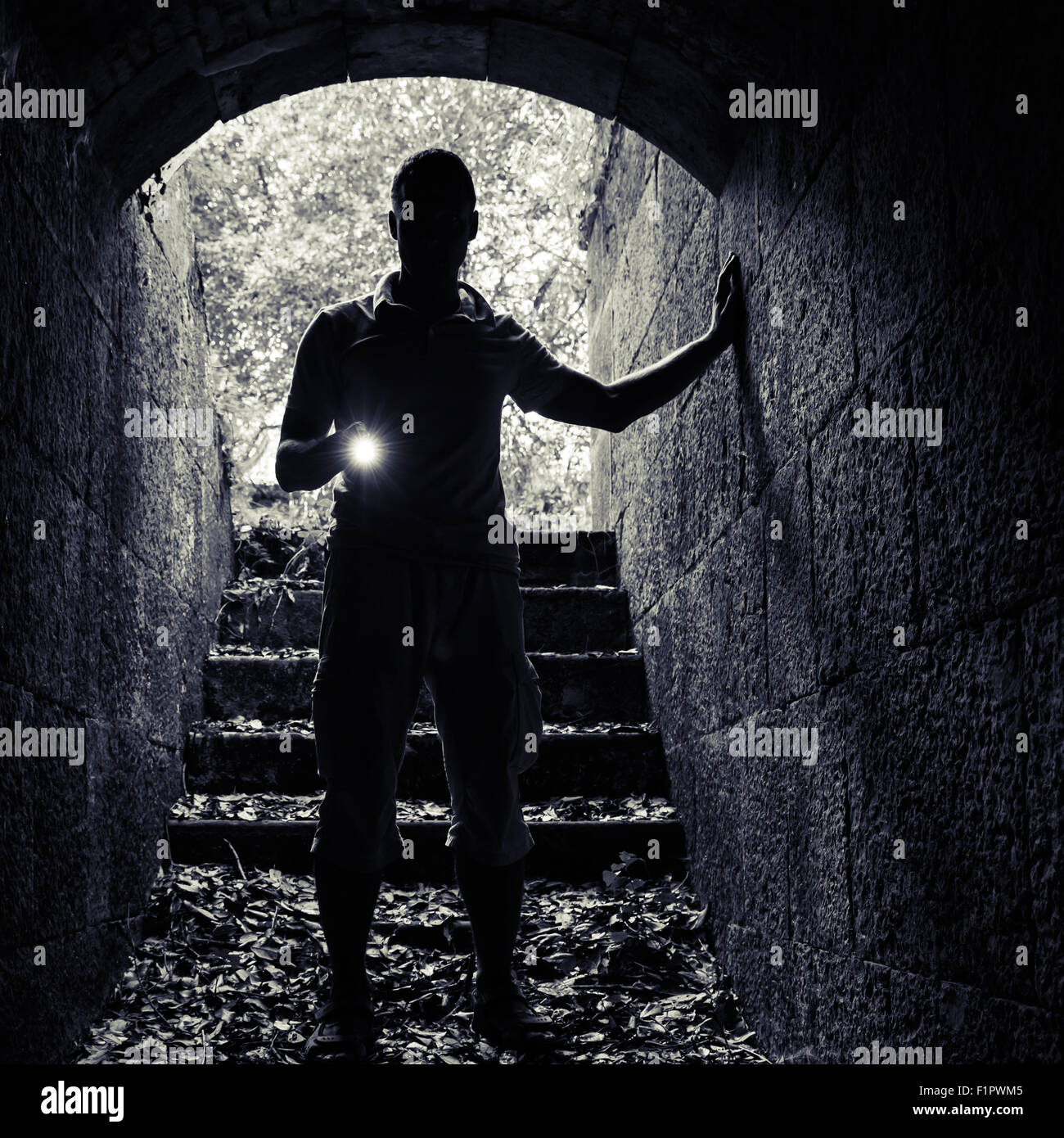 Giovane con una torcia elettrica entra nel tunnel di pietra e guarda al buio, foto quadrata Foto Stock