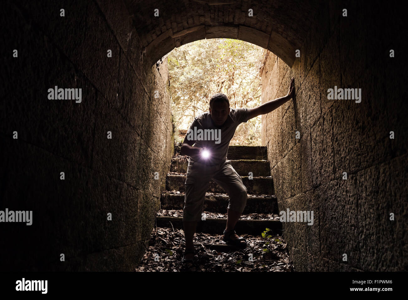 Giovane con una torcia elettrica entra nel tunnel di pietra e guarda al buio, calde tonalità foto effetto filtro Foto Stock
