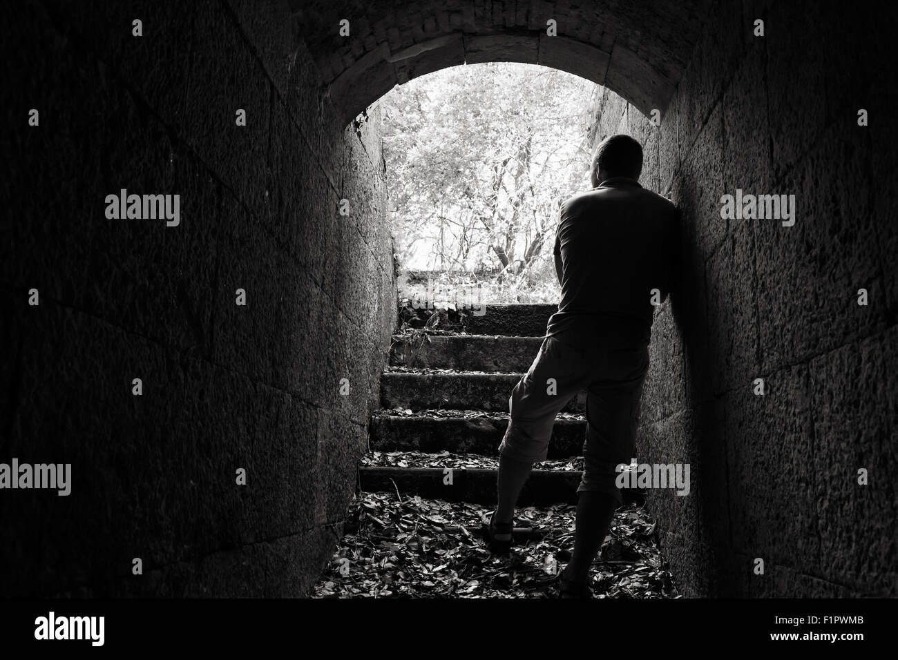 Giovane uomo sorge in pietra scura tunnel con estremità incandescente, foto in bianco e nero Foto Stock