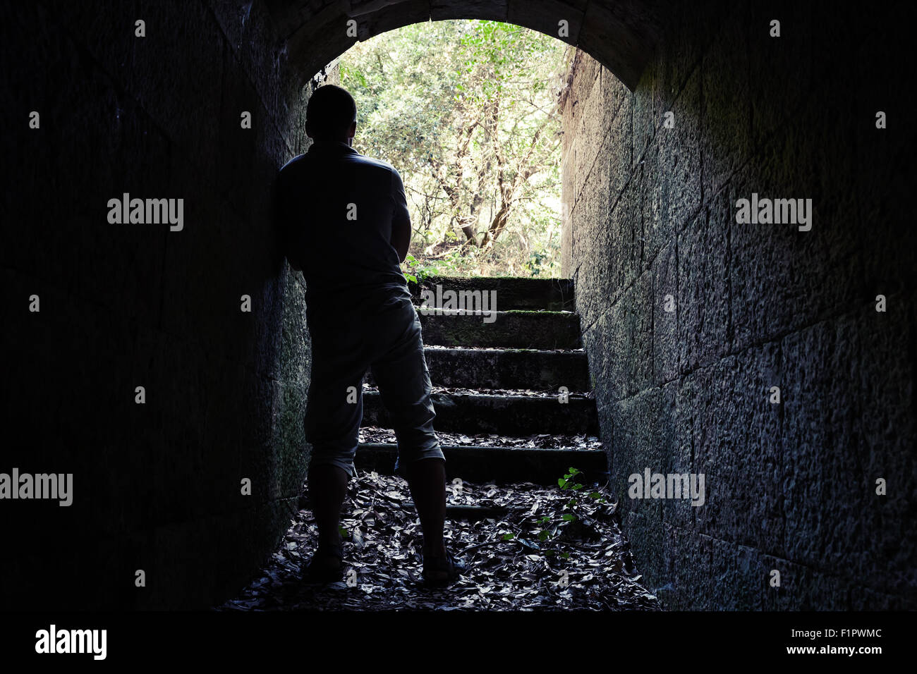 Giovane uomo sorge in pietra scura tunnel con estremità incandescente, vintage la correzione delle tonalità effetto di filtro Foto Stock