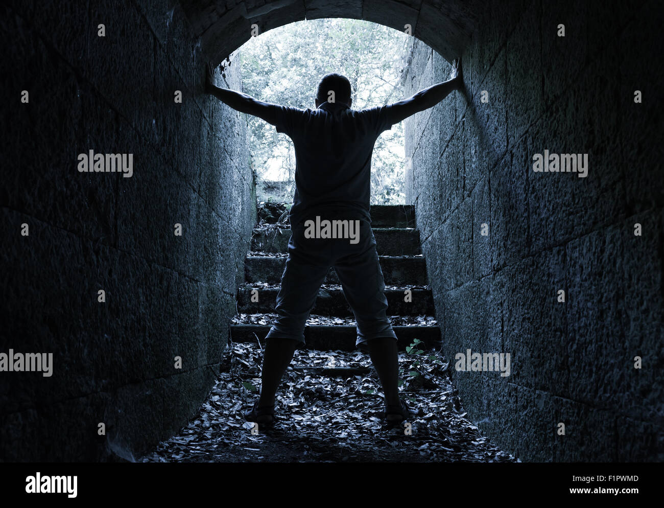 Giovane uomo sorge in pietra scura tunnel con estremità incandescente, tonalità blu del filtro di correzione Foto Stock