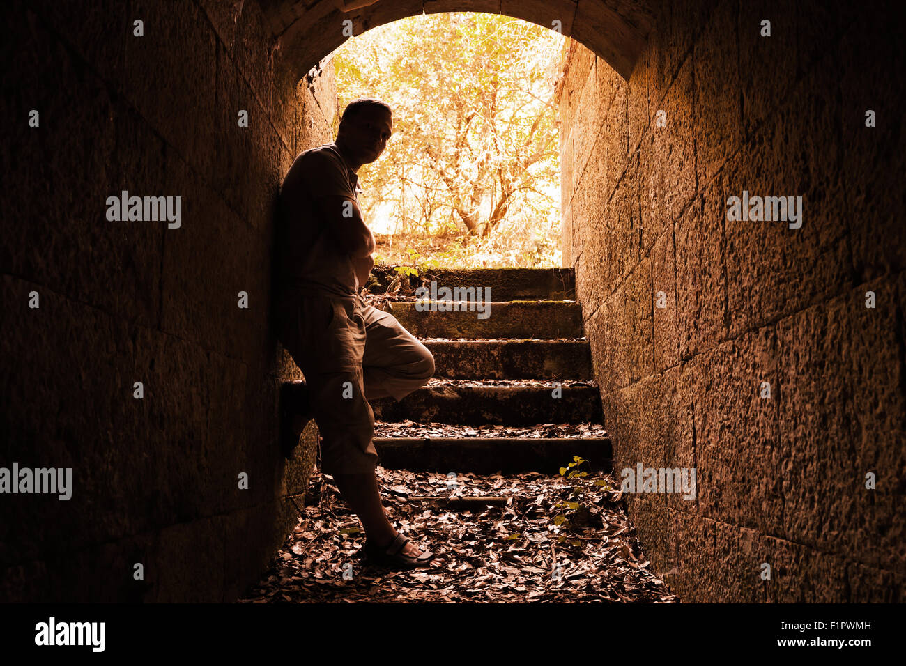 Giovane uomo sorge in pietra scura tunnel con estremità incandescente, la calda tonalità del filtro di correzione Foto Stock