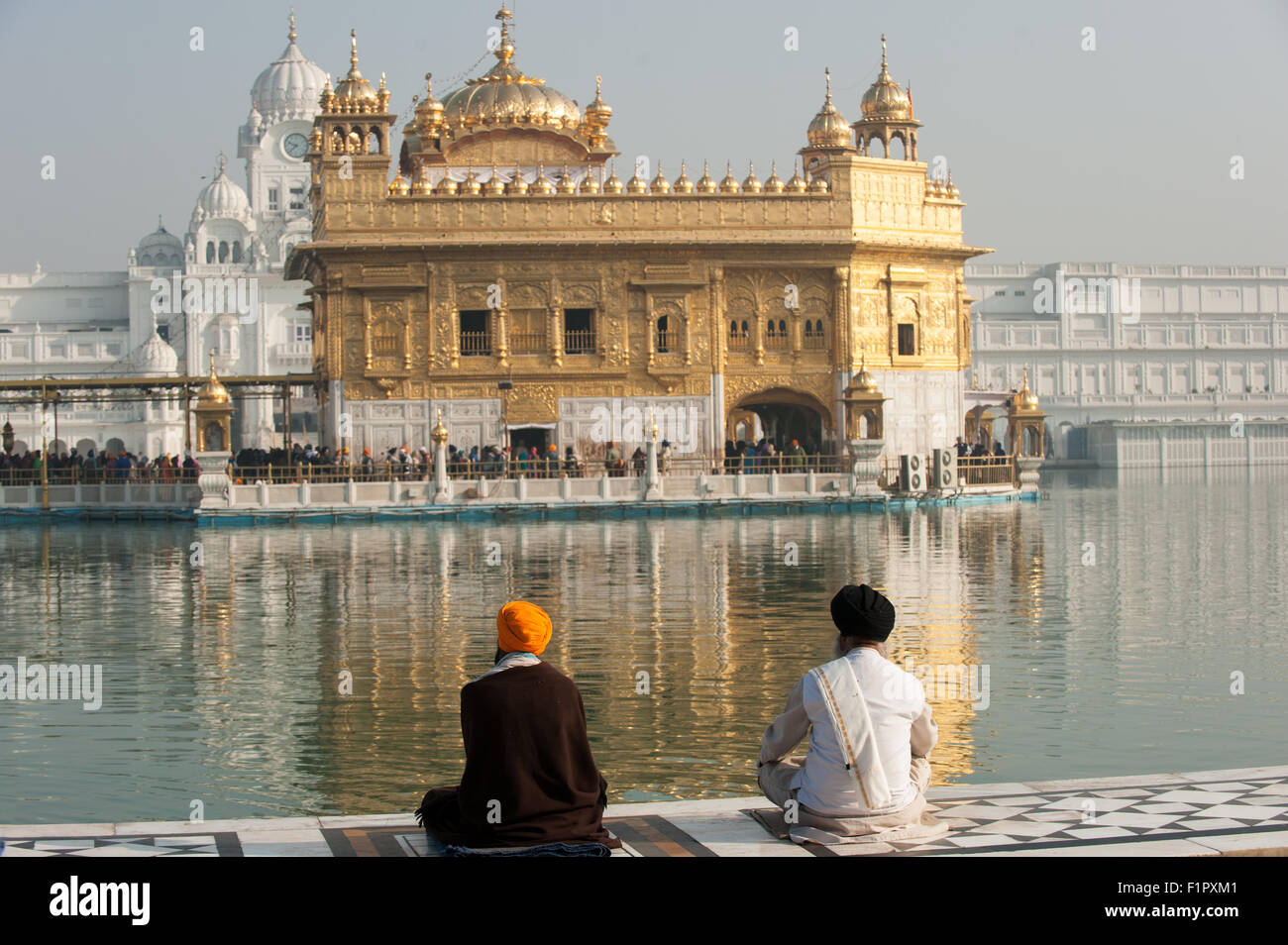 Amritsar Punjab, India. Il Tempio d'Oro - Harmandir Sahib - con due uomini Sikh seduto a gambe incrociate accanto all'acqua santa di l'Amrit Sarovar lago, guardando l'Harmandir Sahib tempio. Foto Stock