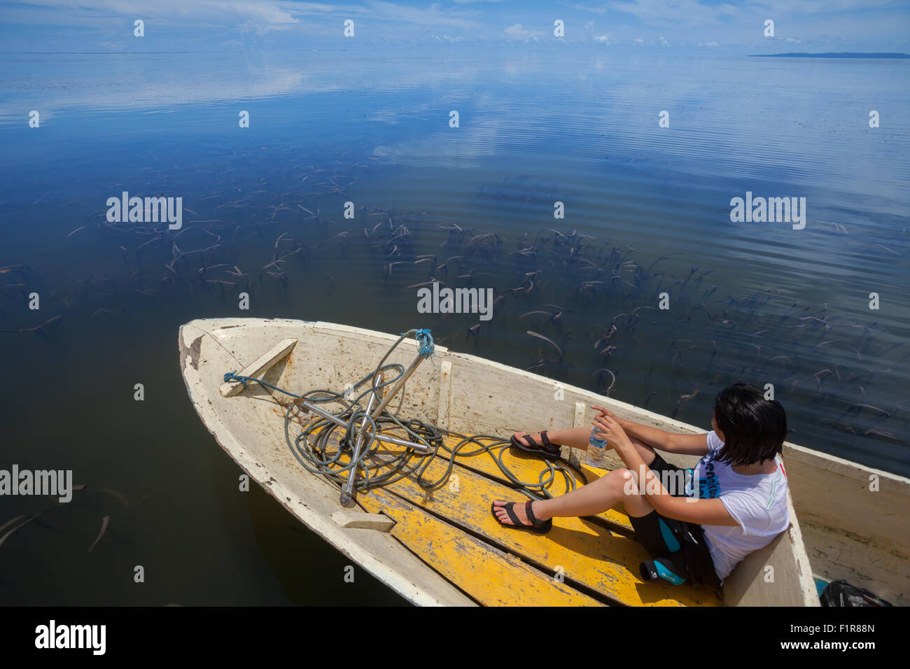 Un giornalista viene fotografato in barca, affacciato sul letto di una prora di mare sulle acque poco profonde vicino all'isola di Marsegu a Seram occidentale, Maluku, Indonesia. Foto Stock