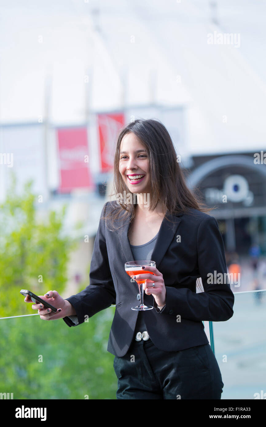 Giovani Latinoamericani/Latin business donna con un telefono cellulare e un cocktail di benvenuto Foto Stock