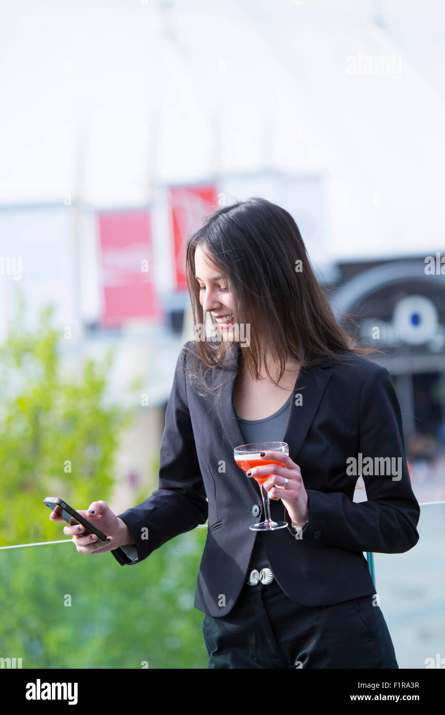 Giovani Latinoamericani/Latin business donna con un telefono cellulare e un cocktail di benvenuto Foto Stock