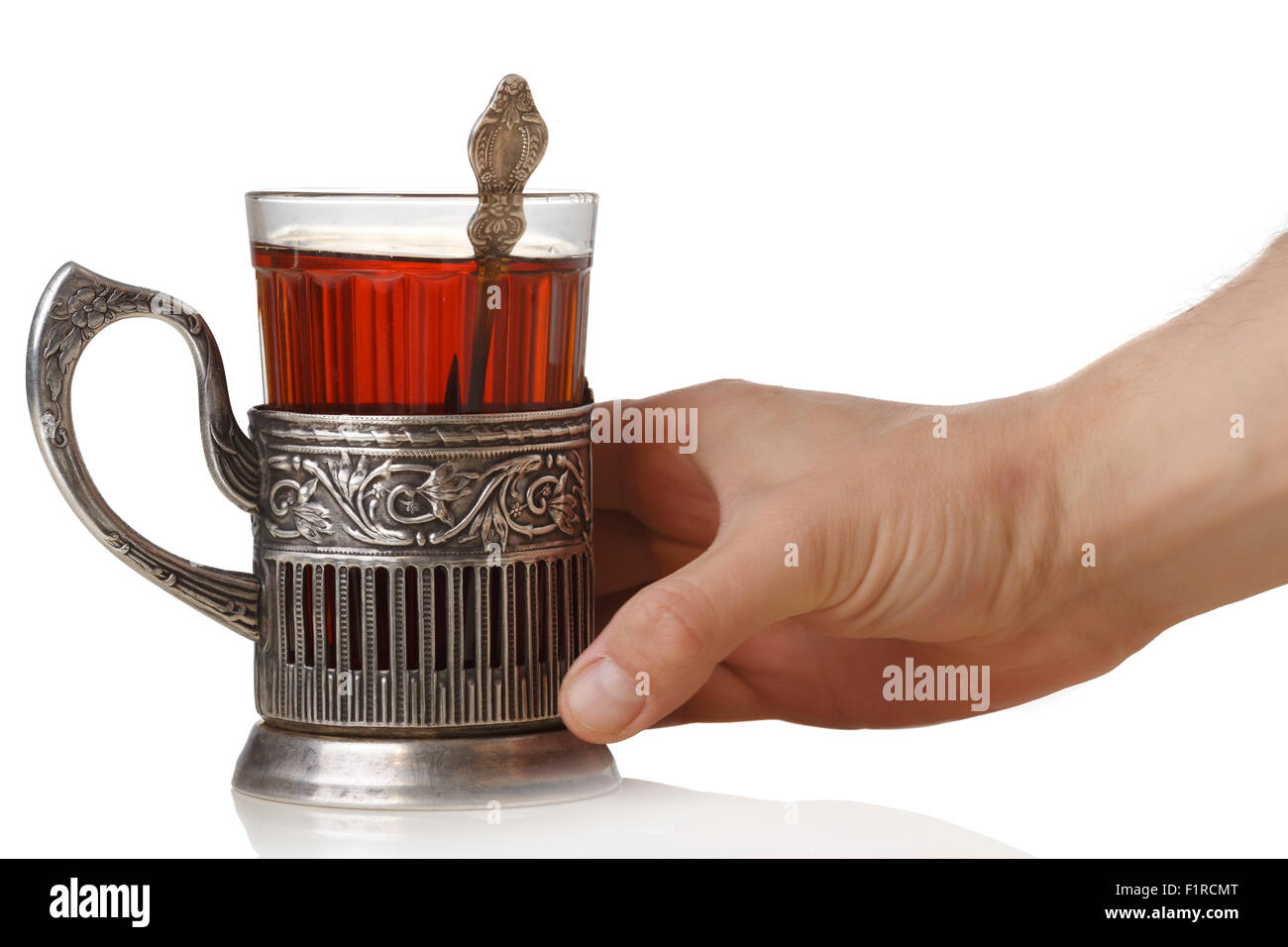 Mano d'uomo tenendo un sovietico vetro sfaccettate di tè (stakan) con cucchiaino in piedi in vetro vintage-titolare (podstakannik) Foto Stock