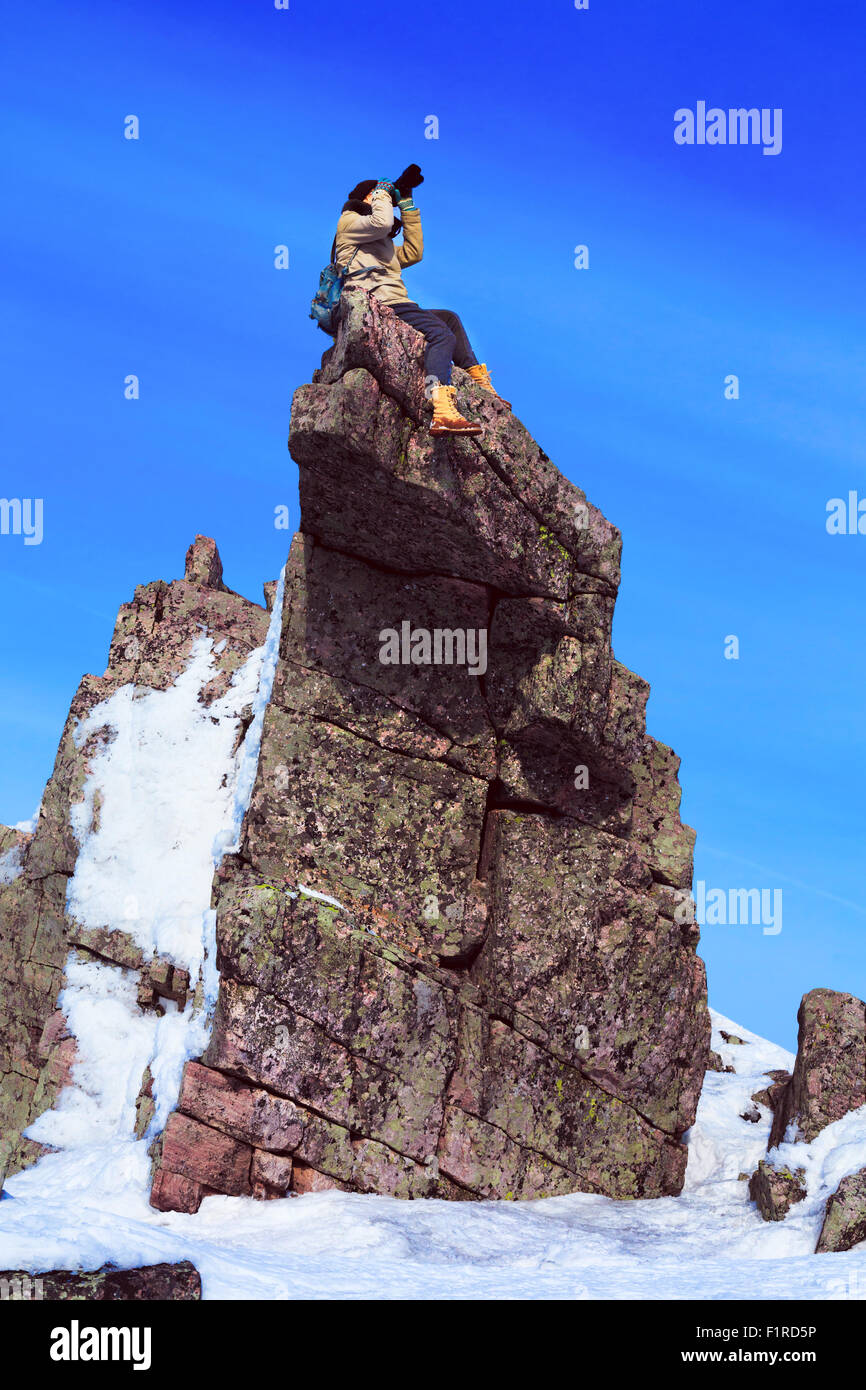 Avventuroso fotografo femmina è seduta su un pinnacolo di roccia durante la ripresa. Viaggi, avventuri, ricreazione attiva concetto. Foto Stock