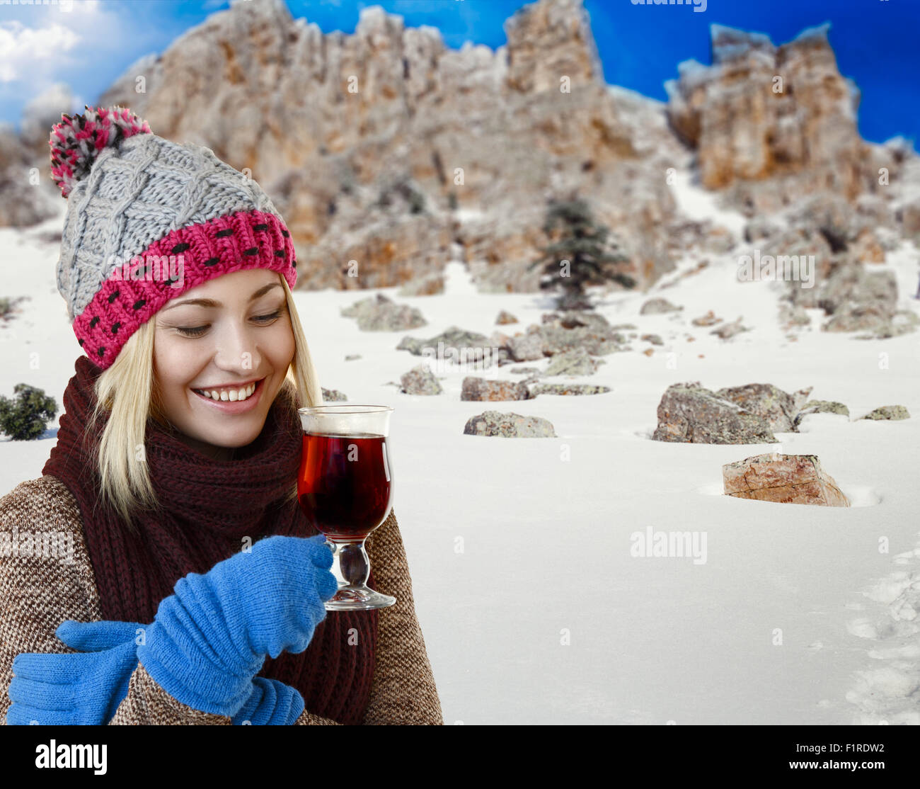 Attraente donna sorridente tenendo una tazza di tè, punch o vin brulé contro inverno sfondo di montagna Foto Stock