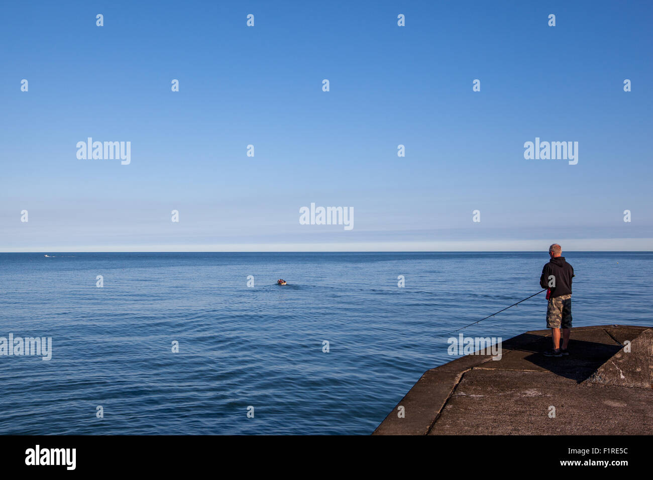 Piccola barca lasciando a riva come sta un uomo sulla fine del molo pesca Foto Stock