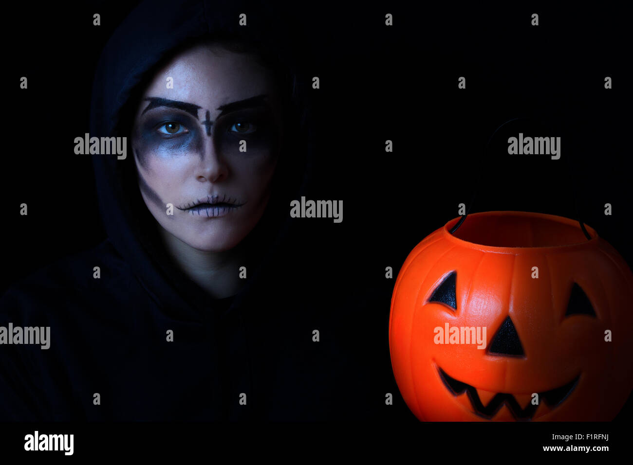 Teen girl in scary faccia tenuta vernice grande contenitore di zucca su sfondo nero. Dolcetto o scherzetto concetto per Halloween Foto Stock
