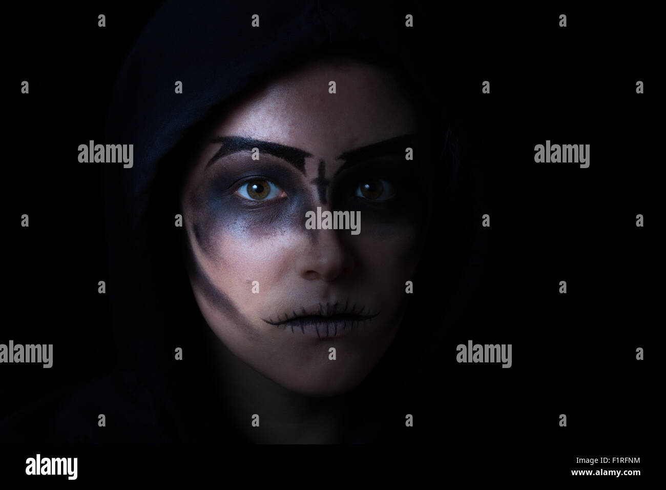 Teen girl indossando il cofano con scary viso trucco su sfondo nero. Foto Stock