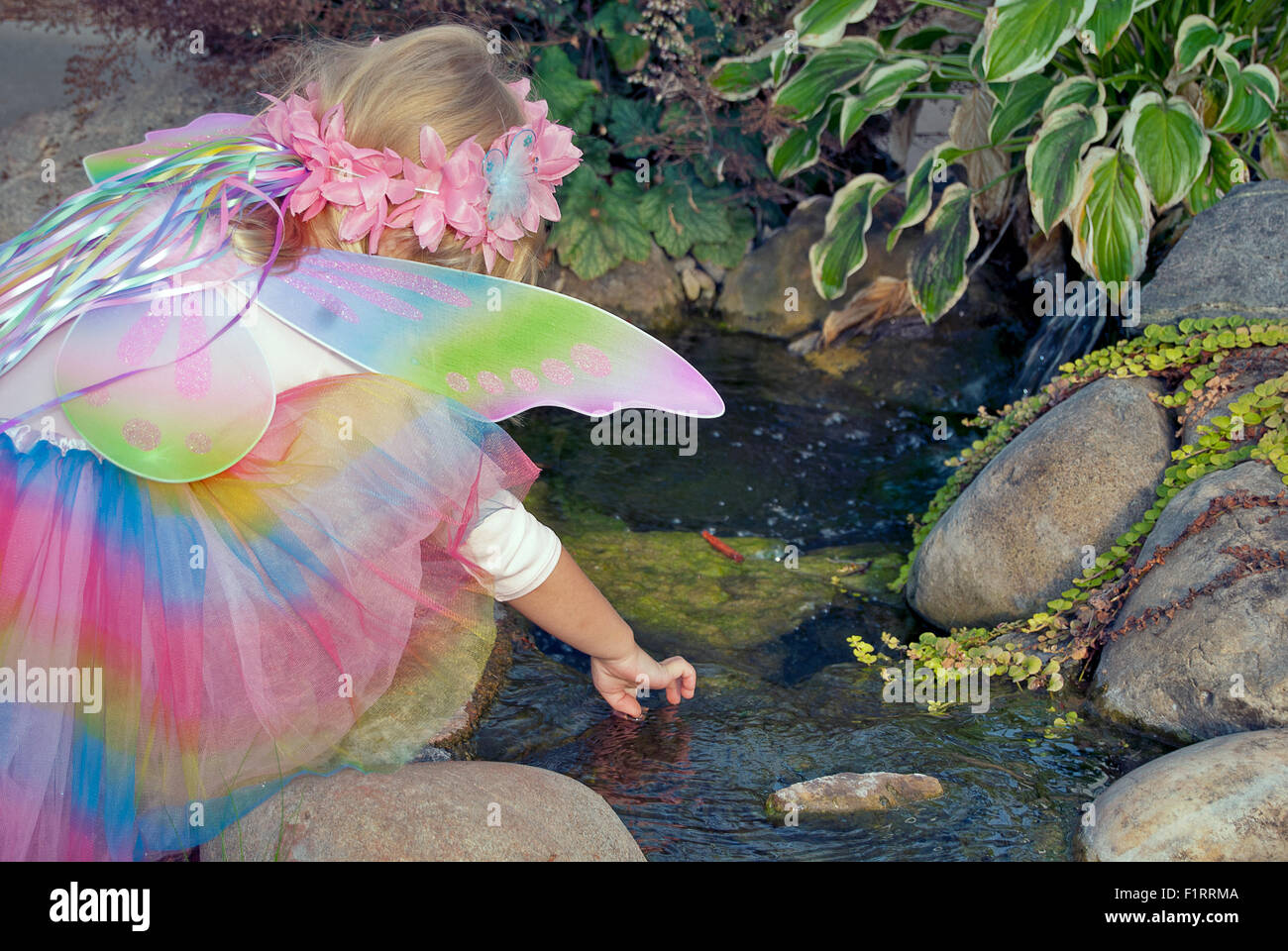 Bimba bionda che indossa un costume fata nel giardino di roccia. Foto Stock