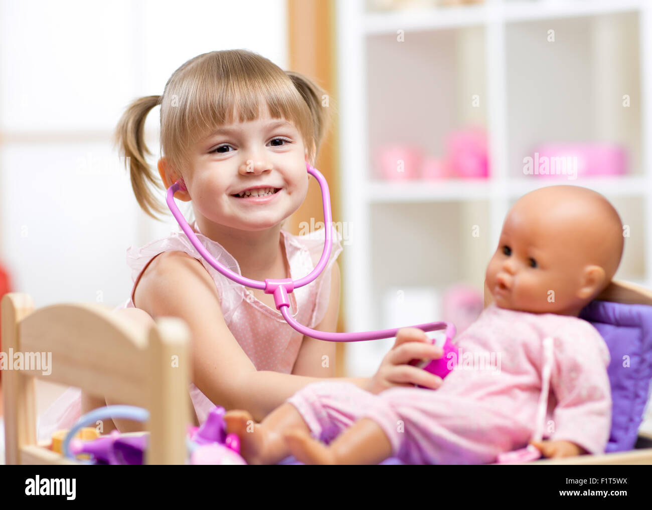 Bambino che gioca medico gioco di ruolo examinating sua bambola utilizzando uno stetoscopio seduti in una sala giochi a casa, a scuola o asilo nido Foto Stock
