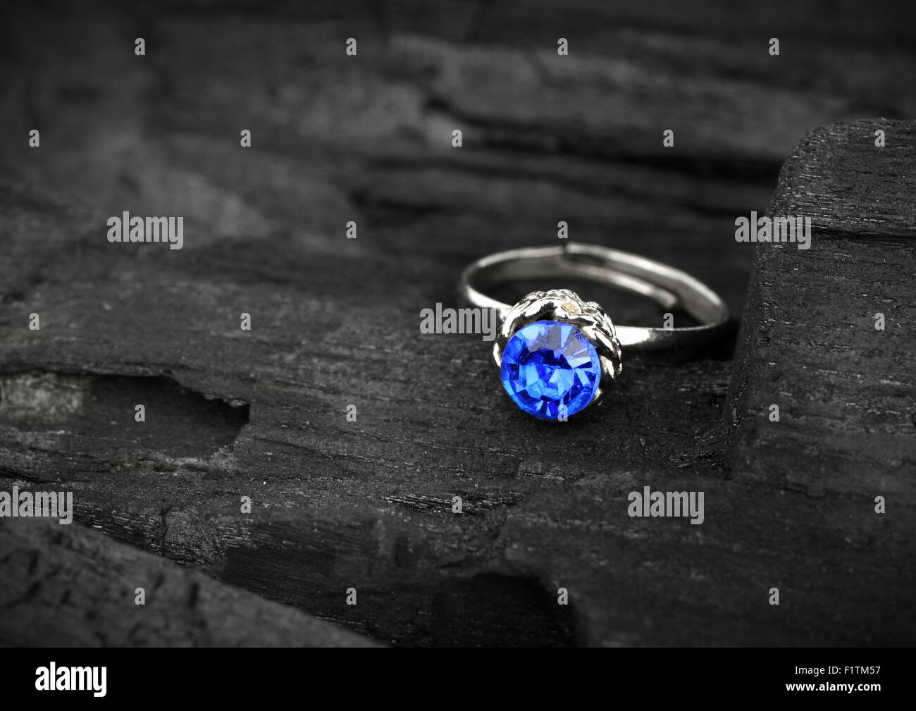 Anello di gioielli witht sapphir blu scuro su sfondo di carbone, soft focus Foto Stock