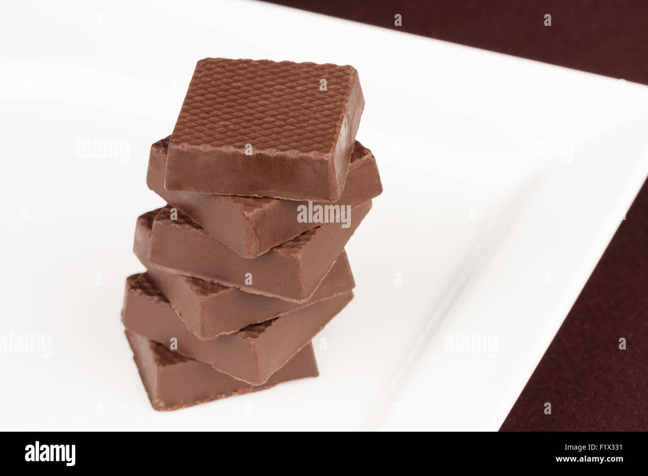 Cioccolato fondente piazze impilati verticalmente su un vassoio bianco Foto Stock