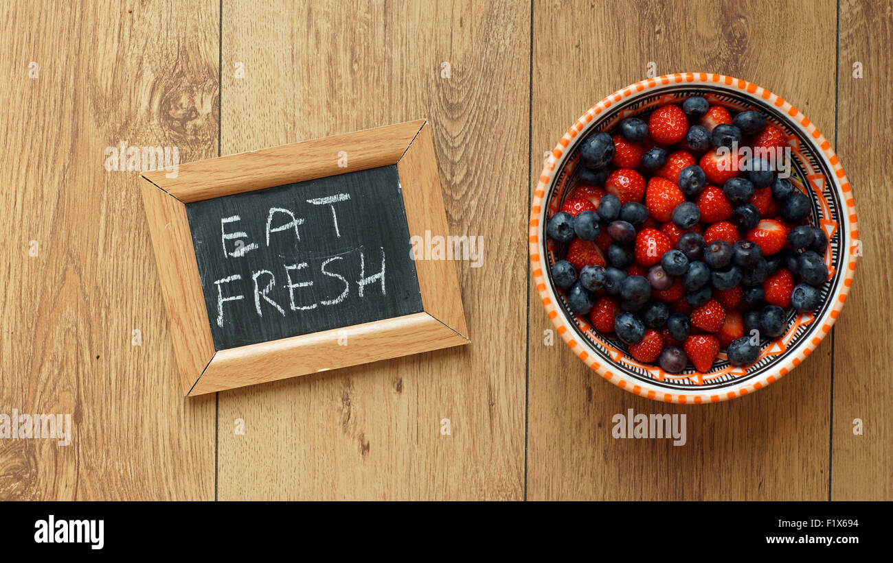 Mangiare fresche scritto su una lavagna accanto ai frutti di bosco e fragole Foto Stock