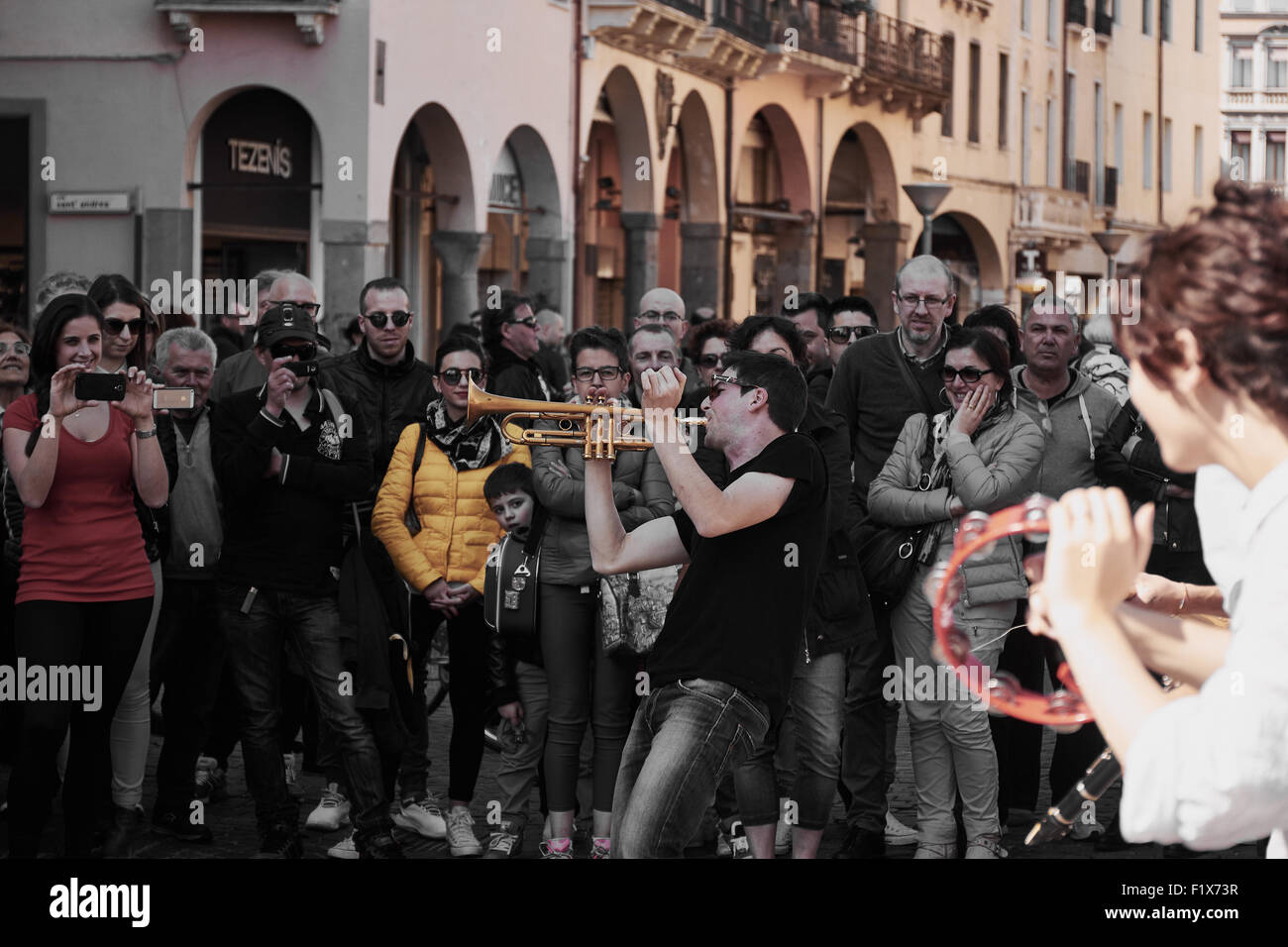 Focus sul musicista di strada a suonare la tromba guardato da una folla di persone con la ragazza che gioca il tamburello in primo piano Padova Italia Foto Stock
