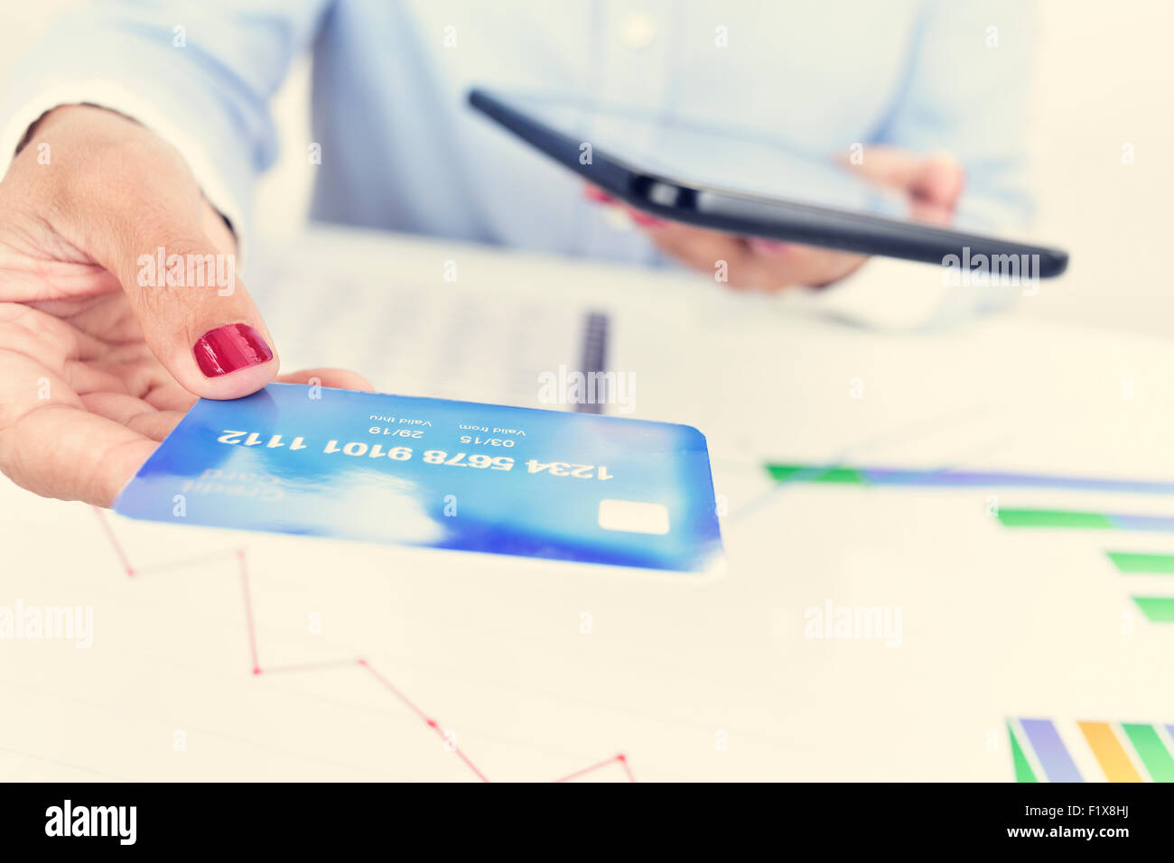 Primo piano di una giovane donna nel suo ufficio con una carta di credito in una mano e un computer tablet nell'altra mano Foto Stock