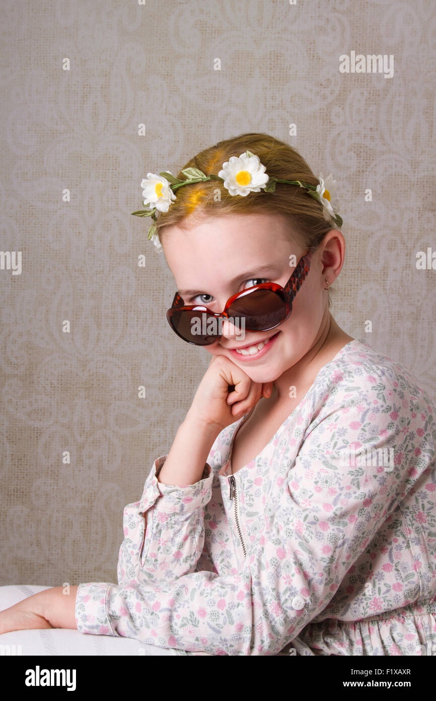 Ragazza giovane con fiori nel suo pelo giallo, posa per la fotocamera con un paio di occhiali da sole. Foto Stock