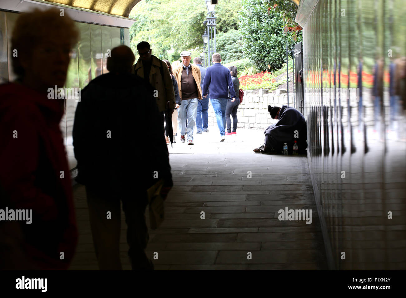 Un senzatetto di sesso maschile seduto a mendicare ma guardando verso il basso e fuori in un sottopassaggio che si trova nel centro di Londra come la gente passa da su un affollato pranzo ignorando l'uomo Foto Stock