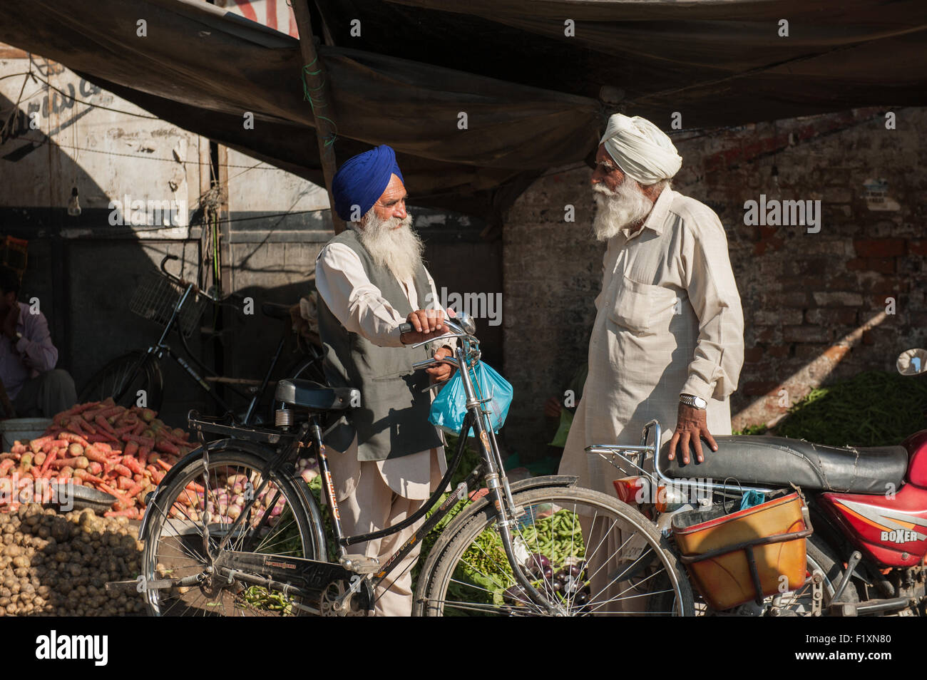 Amritsar Punjab, India. Due i sikh di parlare al mercato con noleggio biciclette e moto. Foto Stock