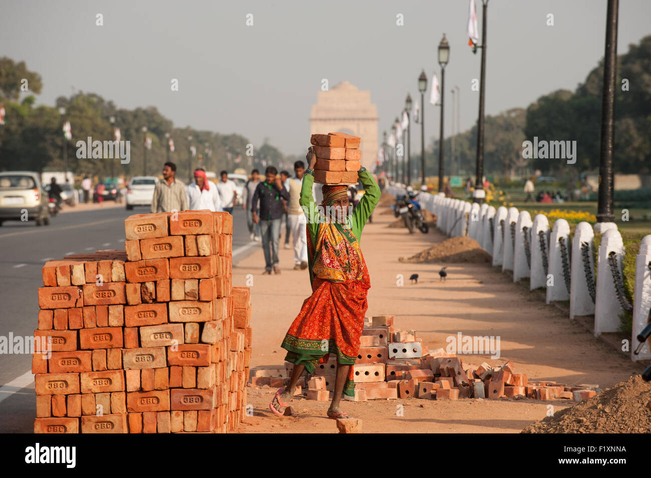 Delhi, India. Una donna operaio portante 8 otto mattoni sul suo capo da un mucchio di mattoni a lato della strada vicino alla porta dell'India. Foto Stock