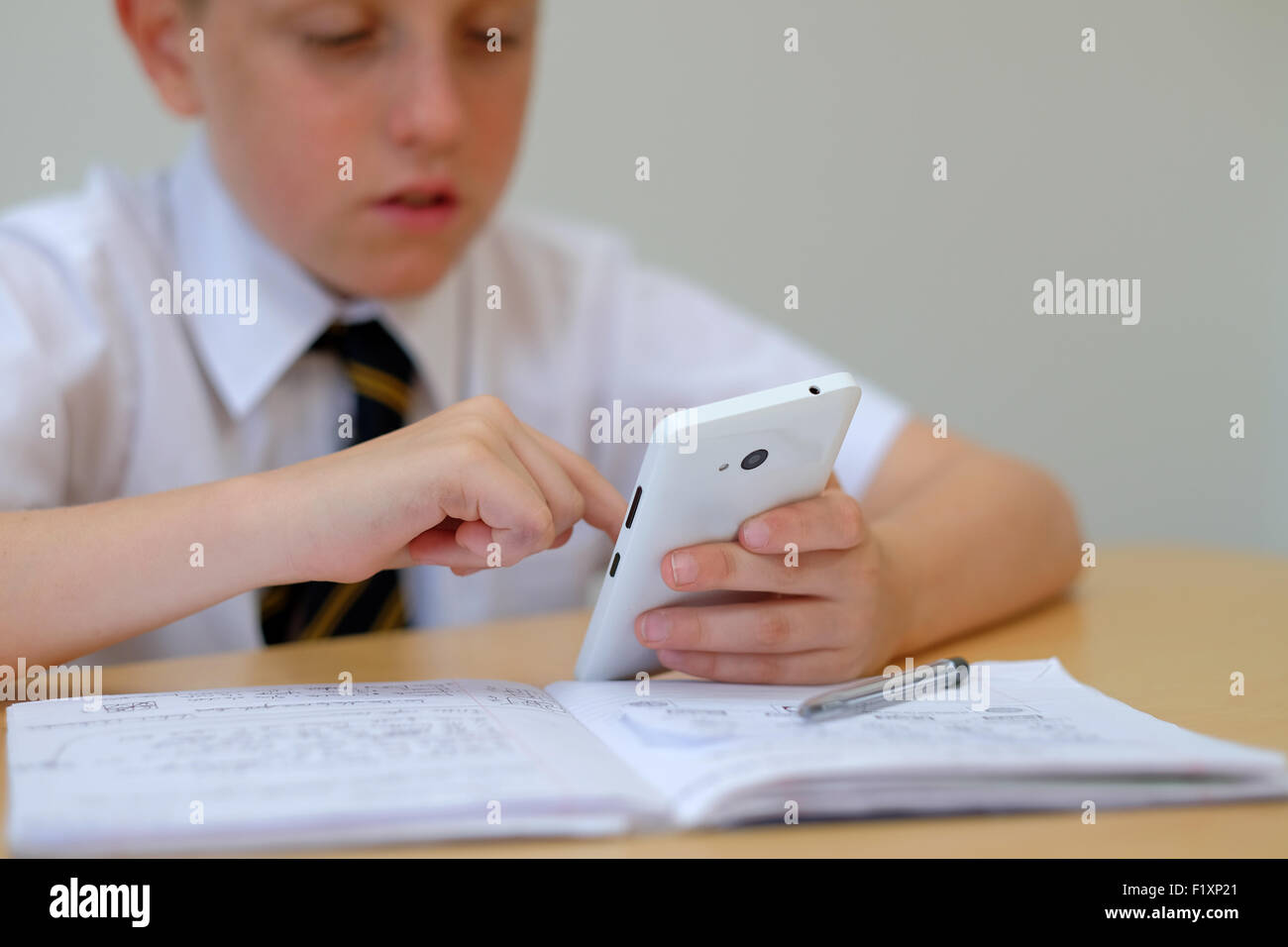 Scolaro distratti da utilizzando un telefono mobile (SMS) mentre è seduto alla sua scrivania con il suo corso di lavoro lavoro home Foto Stock