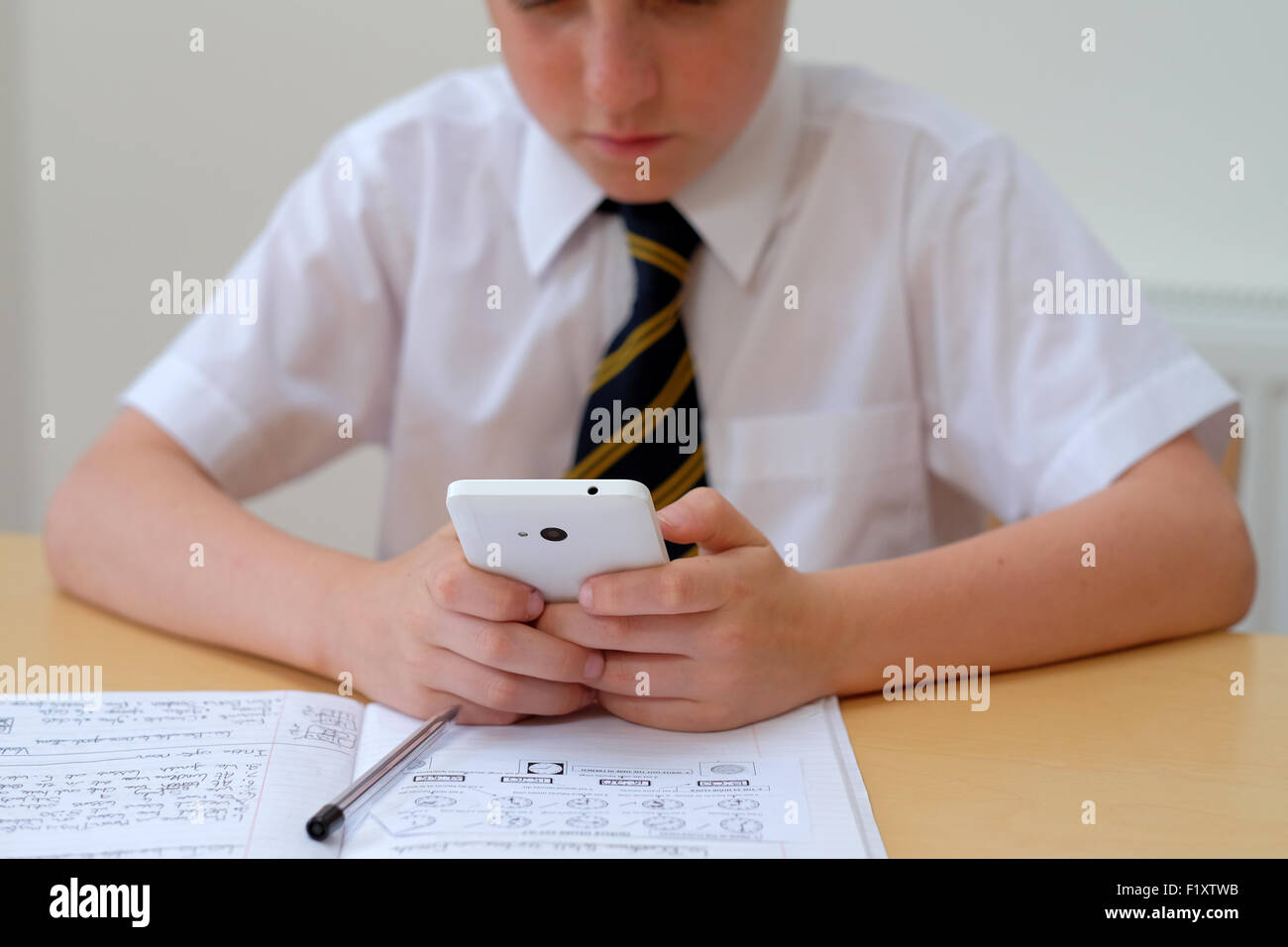 Scolaro distratti da utilizzando un telefono mobile (SMS) mentre è seduto alla sua scrivania con il suo corso di lavoro lavoro home Foto Stock