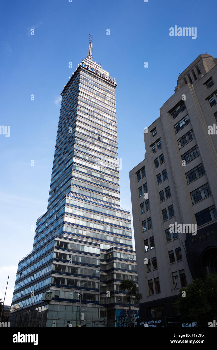 Torre Latinoamericana ad altezza totale Città del Messico | CITTÀ DEL MESSICO, Messico — La Torre Latinoamericana si erge per i suoi 181 metri (594 piedi) completi sopra l'Eje Central Lázaro Cárdenas, il suo fusto in vetro e acciaio visibile dal livello stradale fino all'asta dell'antenna tra i vicini edifici di metà secolo. Completata nel 1956 su progetto di Augusto H. Álvarez, fu tra i primi grattacieli principali costruiti sui terreni argillosi comprimibili del bacino prosciugato del lago Texcoco, progettata su pali profondi per resistere all'attività sismica. Foto Stock