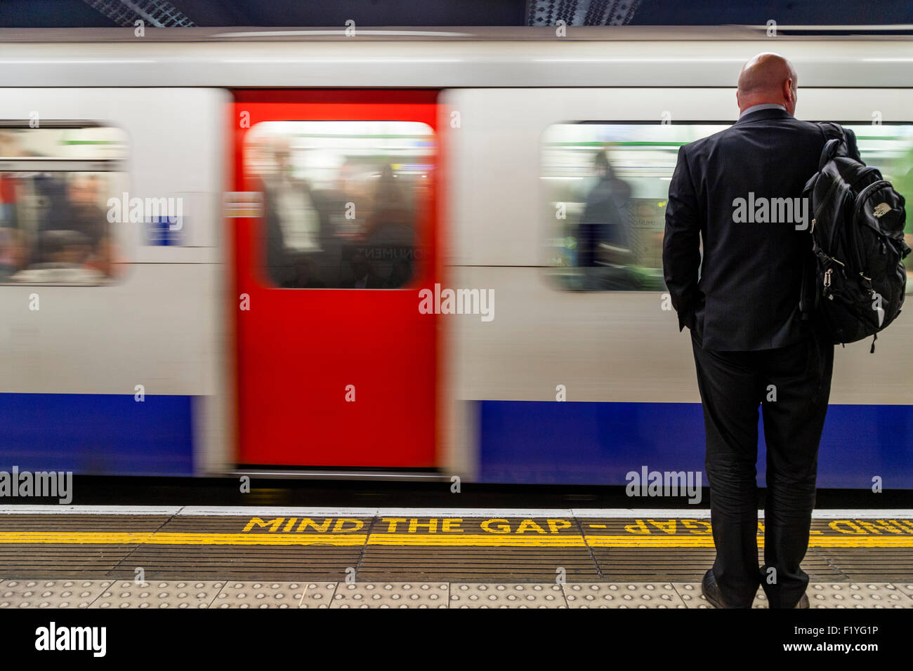 Un business man in una tuta attende un treno della metropolitana di Londra, Londra, Inghilterra Foto Stock