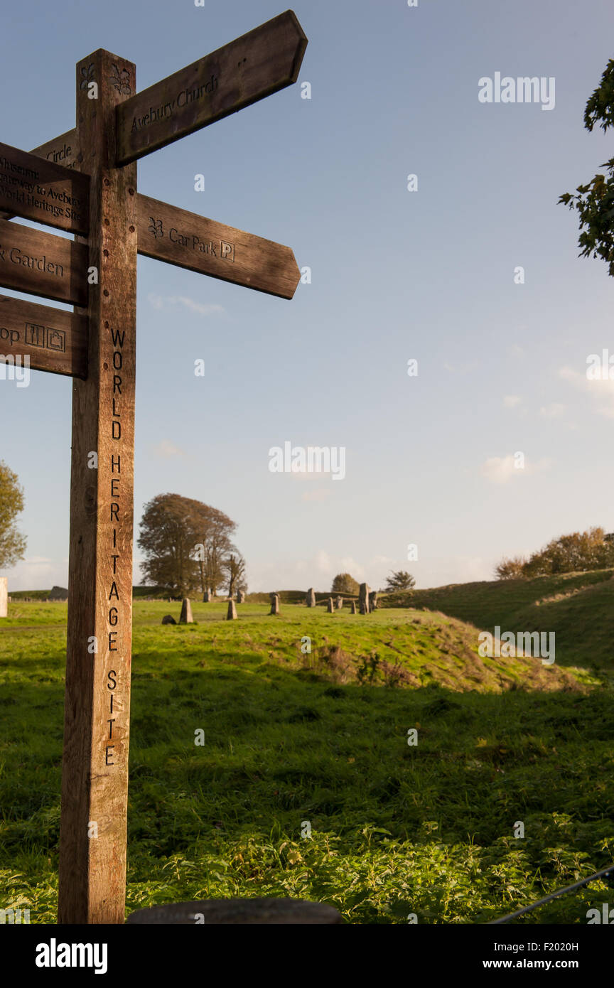 Avebury, Wiltshire. Sentiero fingerpost segno "Sito Patrimonio Mondiale dell'Umanita' con un neolitico cerchio di pietra costruito su una banca eathrwork e fossa. Foto Stock