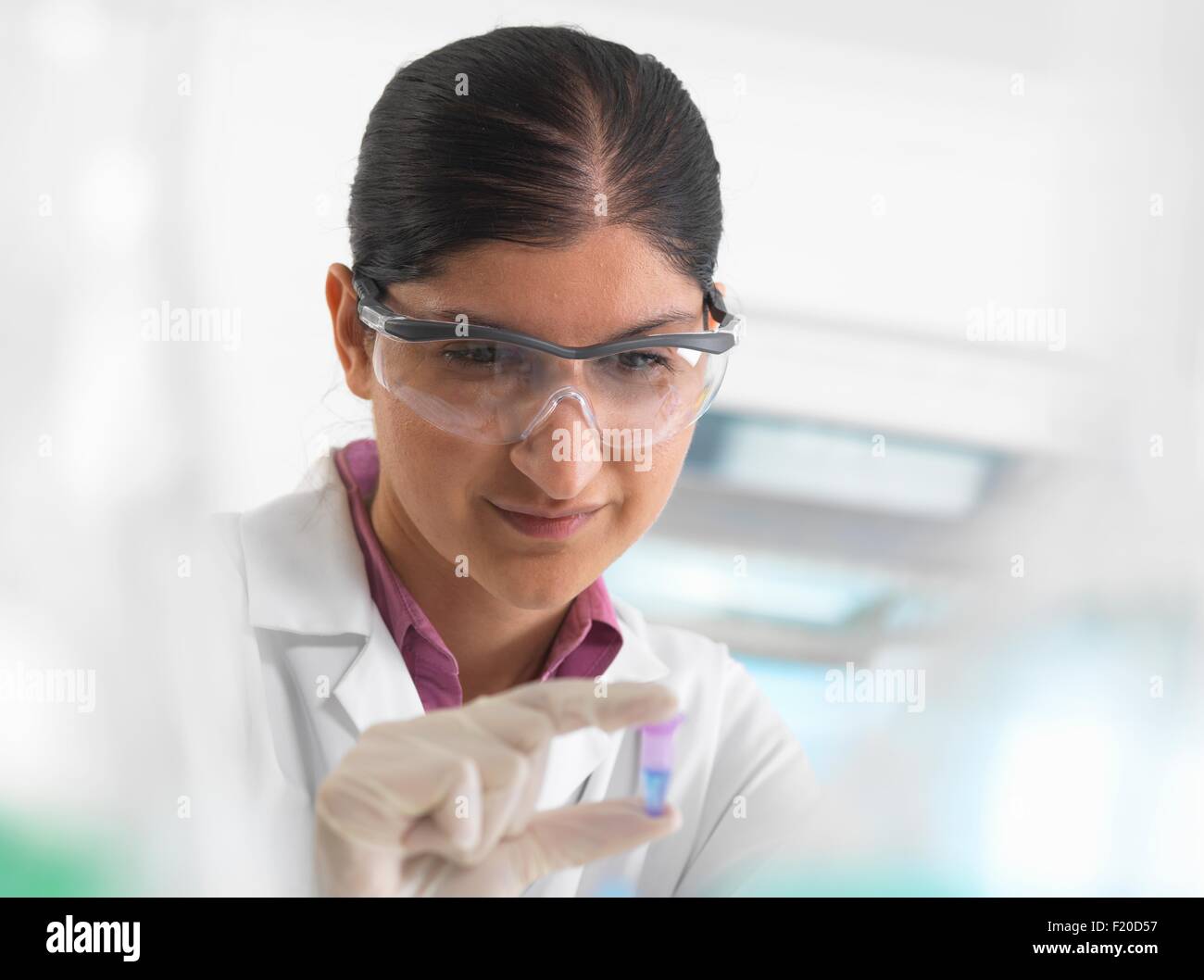 Donna scienziato visualizzazione di campione nella provetta eppendorf davanti a DNA testing in laboratorio. Foto Stock