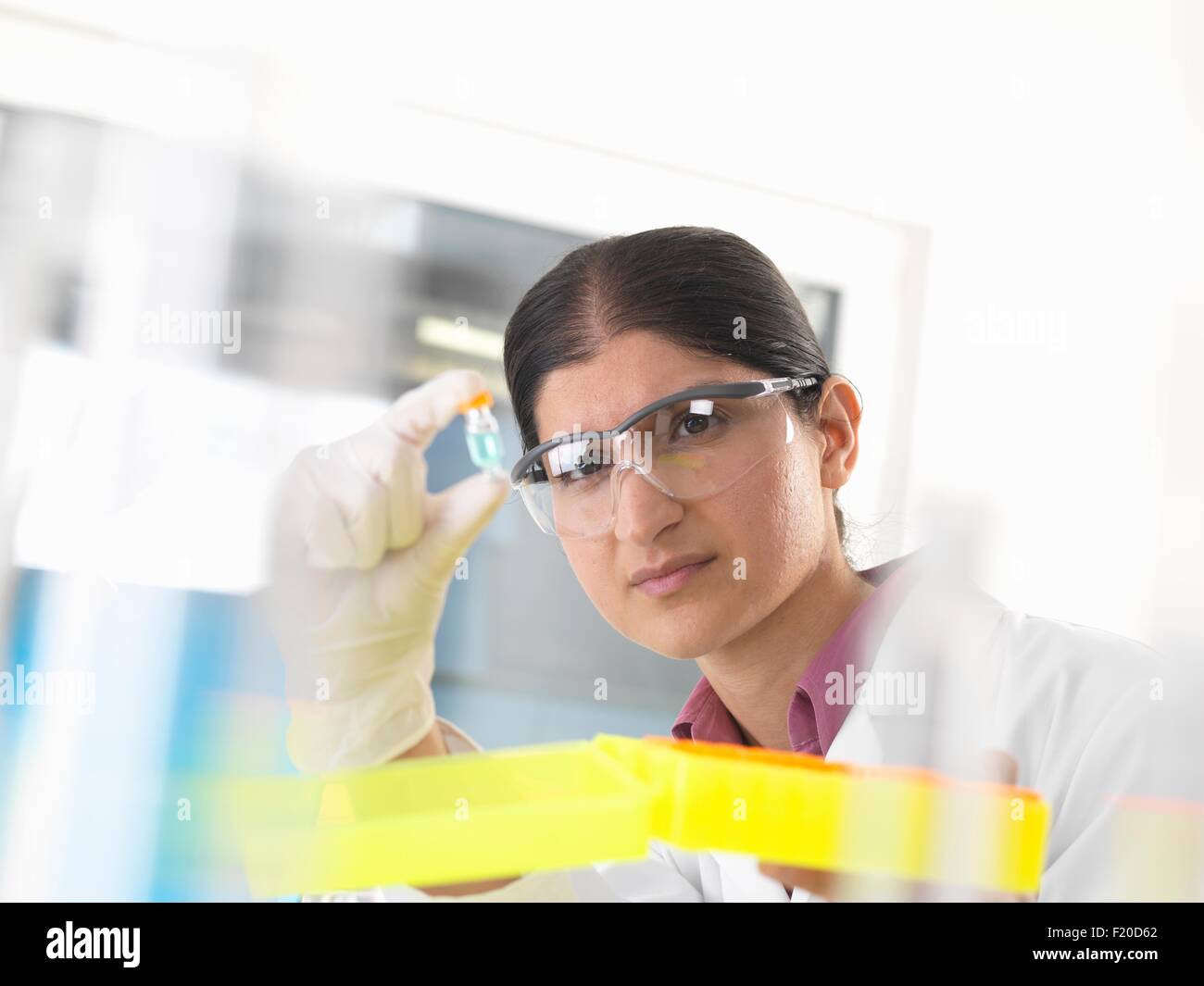 Donna scienziato tenendo premuto fino ed esaminando campione chimico in laboratorio Foto Stock