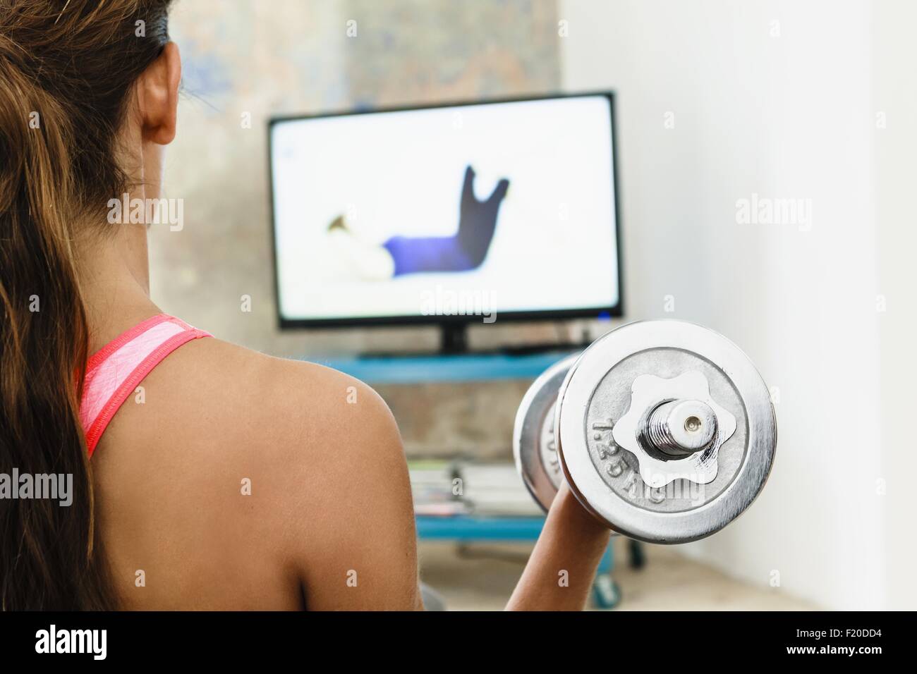 Giovane donna allenamento con i pesi a mano in salotto mentre si guarda lo schermo del computer Foto Stock