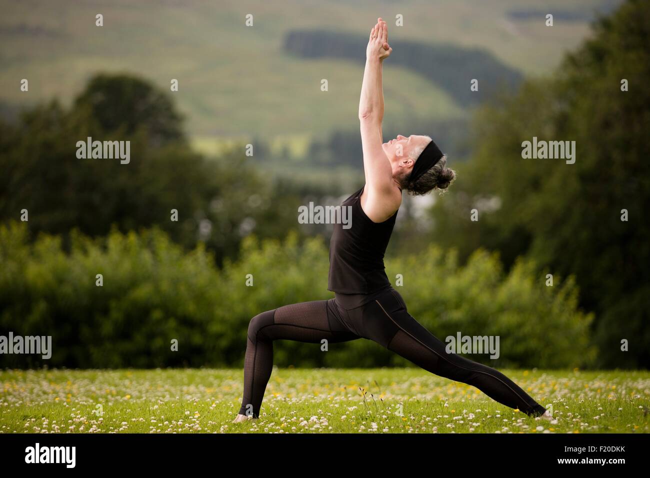 Donna matura la pratica dello yoga warrior posano con bracci sollevati nel campo Foto Stock