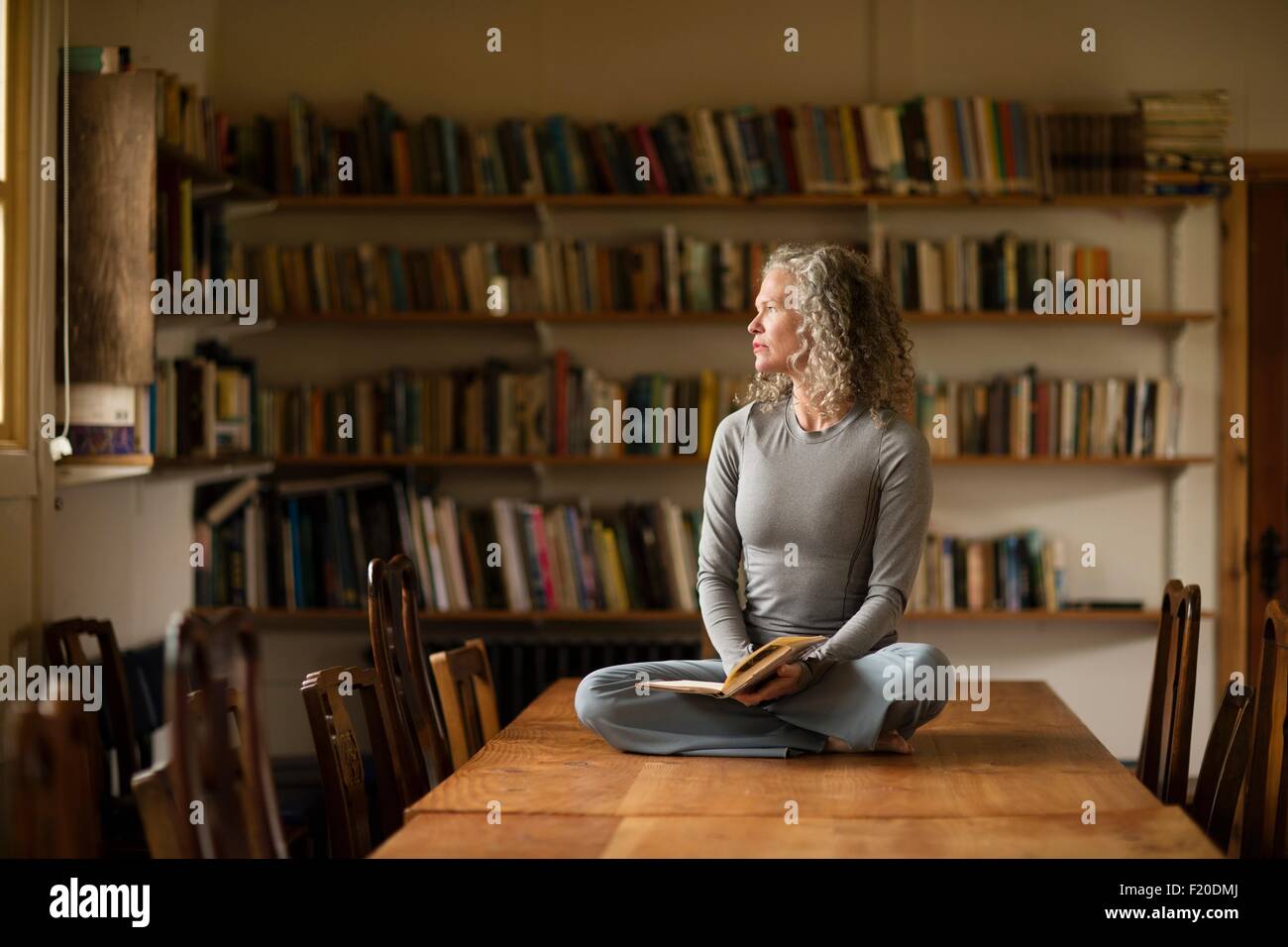 Donna matura seduta zampe trasversale sul tavolo da cucina guardando fuori della finestra Foto Stock