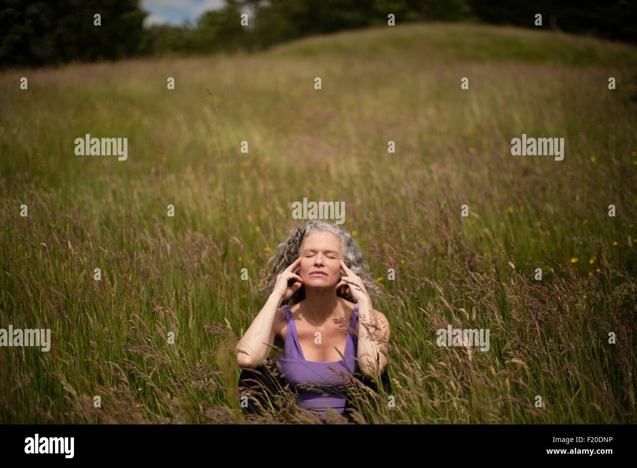 Donna matura con le dita sul suo templi seduto in erba lunga meditazione Foto Stock