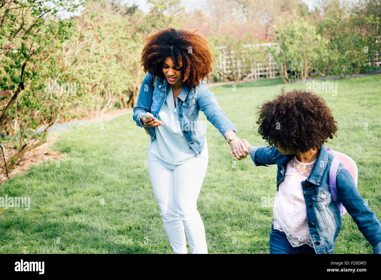 Madre guardando smartphone venga tirato dalla figlia tenendo la mano Foto Stock