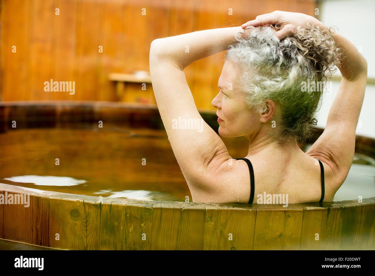 Donna matura con le mani nei capelli nella vasca calda al rifugio eco Foto Stock