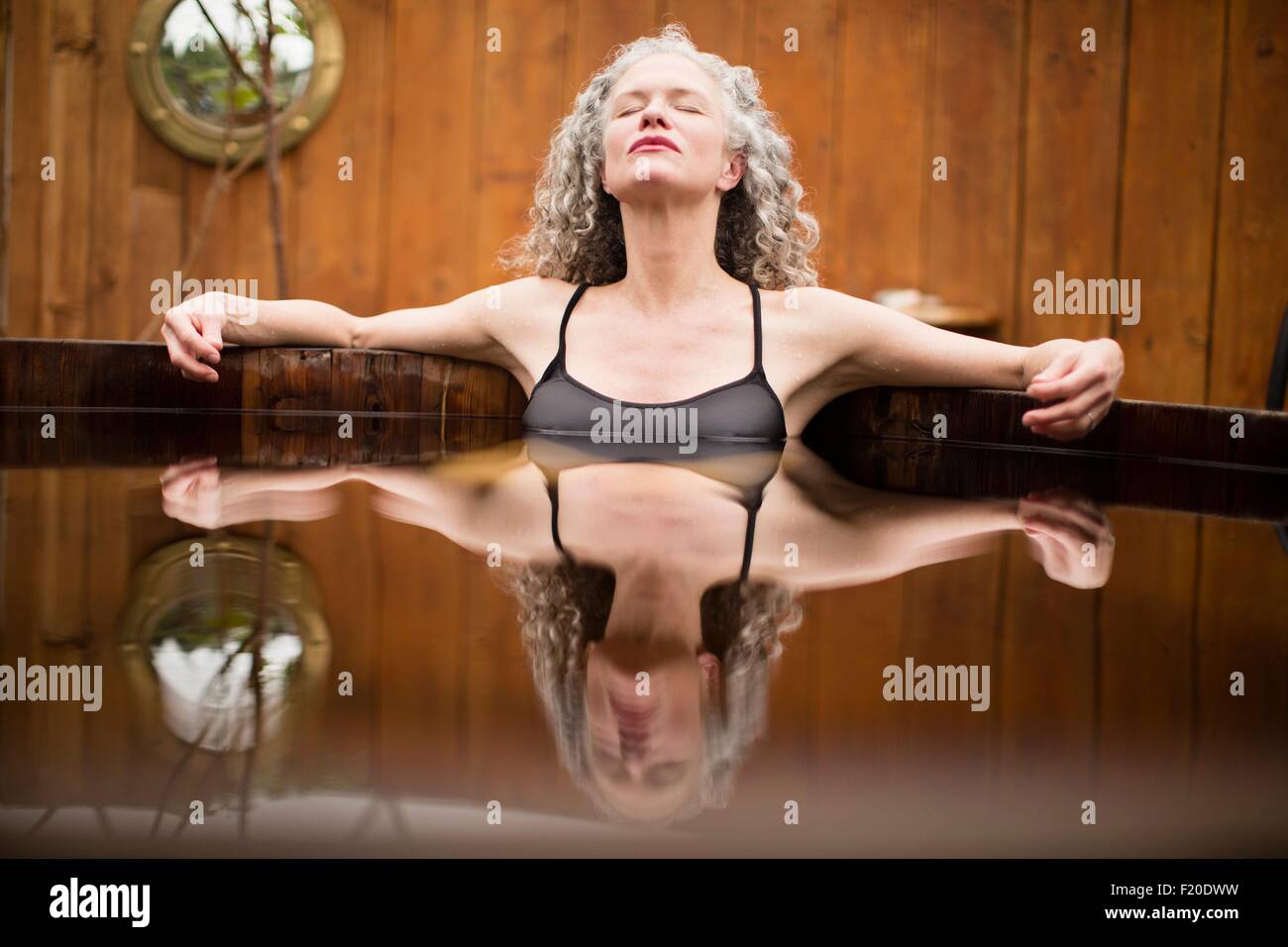 Donna matura meditando con gli occhi chiusi nella vasca calda al rifugio eco Foto Stock