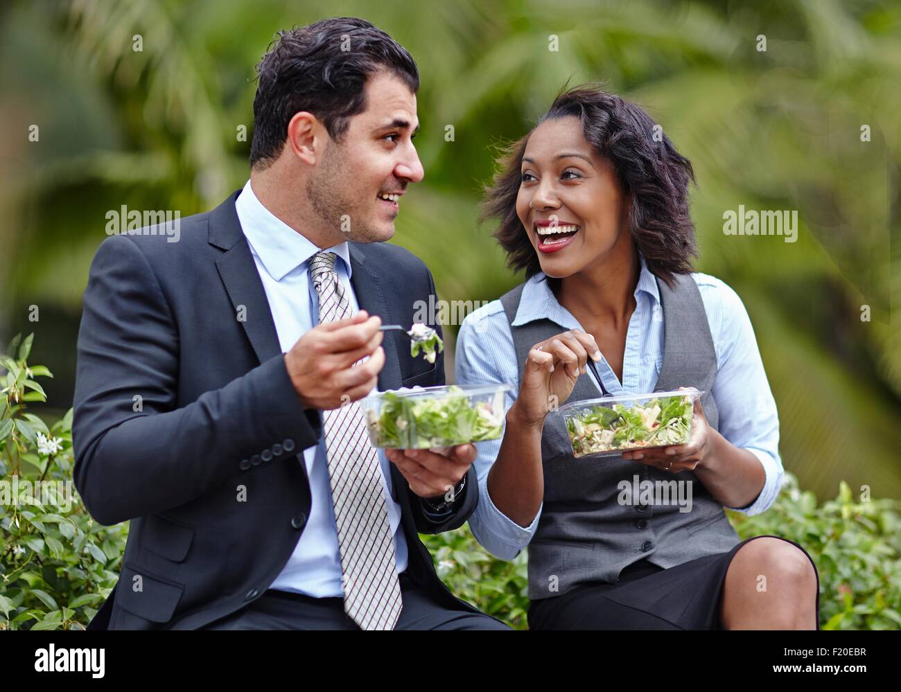 La gente di affari seduti fianco a fianco godendo di un insalata sulla pausa pranzo, faccia a faccia sorridente Foto Stock
