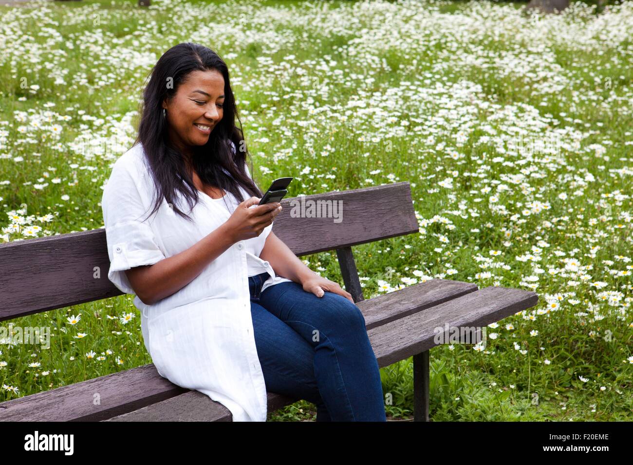 Coppia donna seduta su una panchina nel parco la lettura del testo dello smartphone Foto Stock
