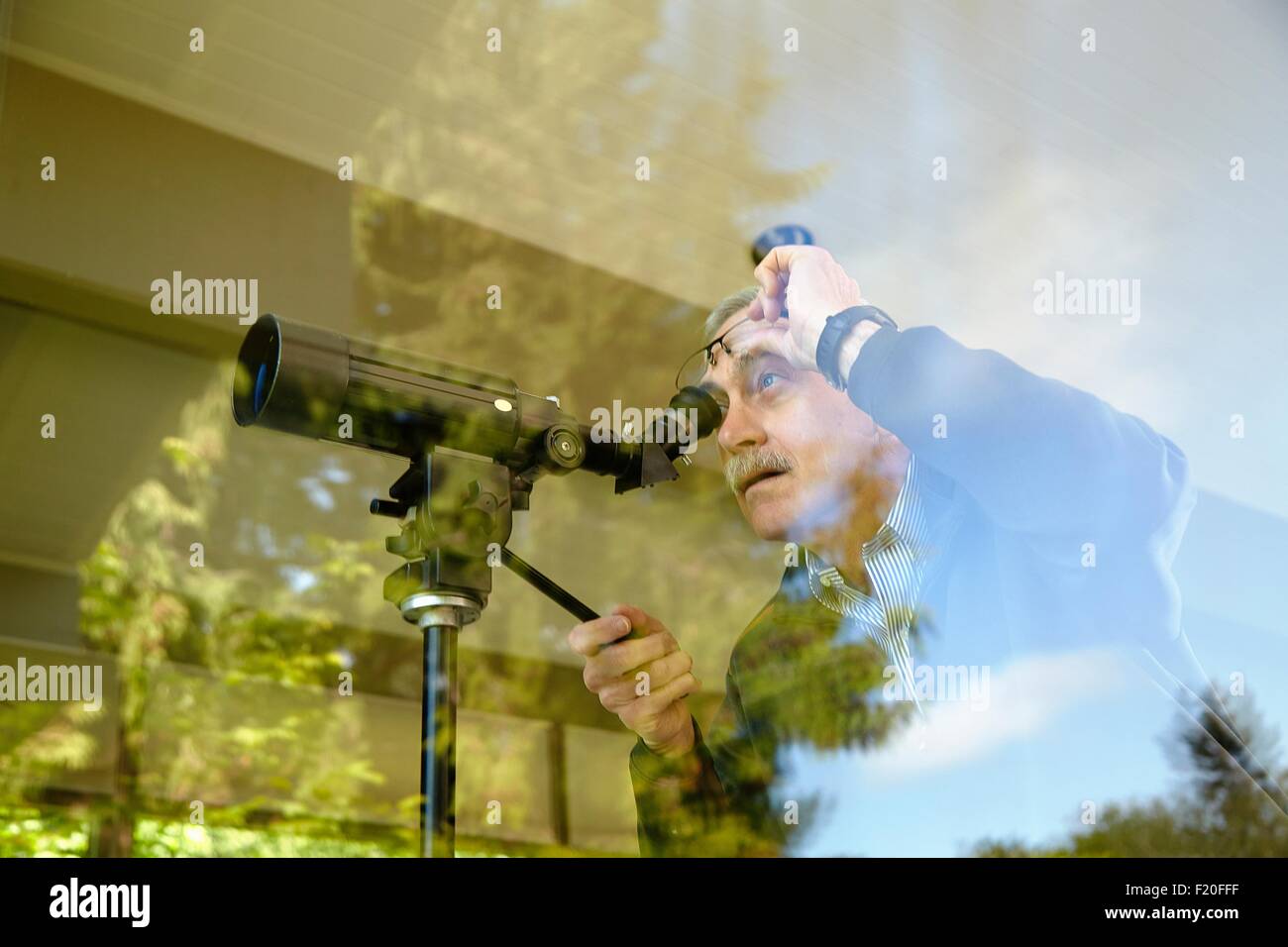 Senior uomo a casa, utilizzando un telescopio attraverso la finestra Foto Stock