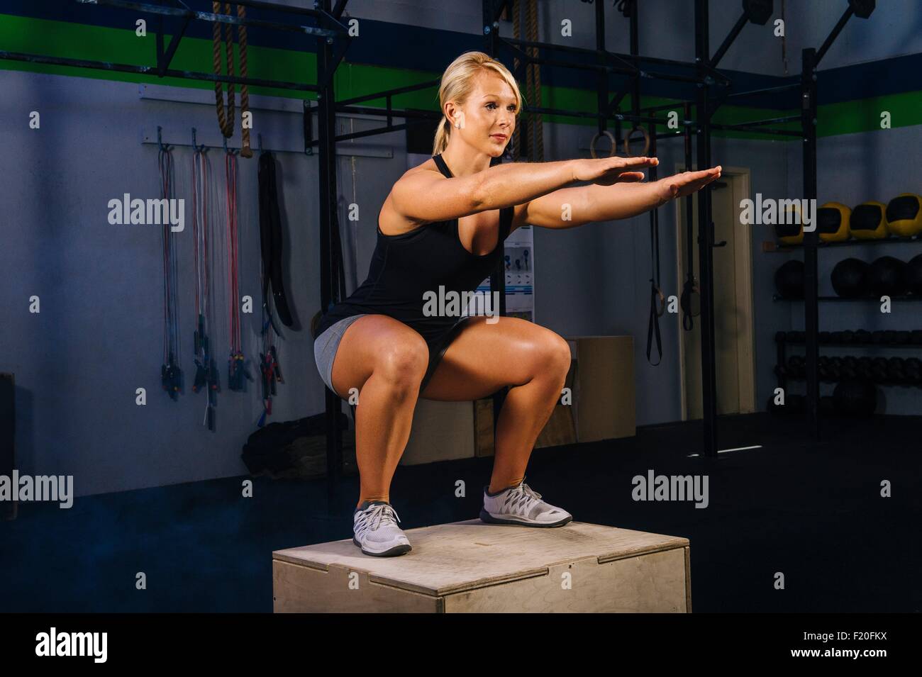 Giovane donna accovacciata sulla casella di palestra con bracci raggiungendo fuori Foto Stock