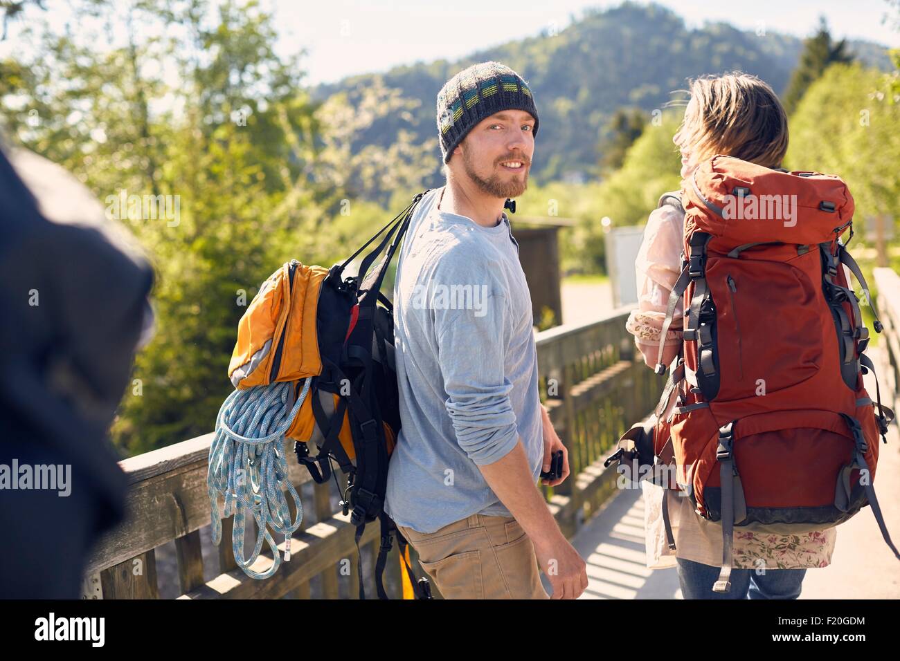 Vista posteriore di escursionisti che trasportano zaini, guardando sopra la spalla, sorridente Foto Stock