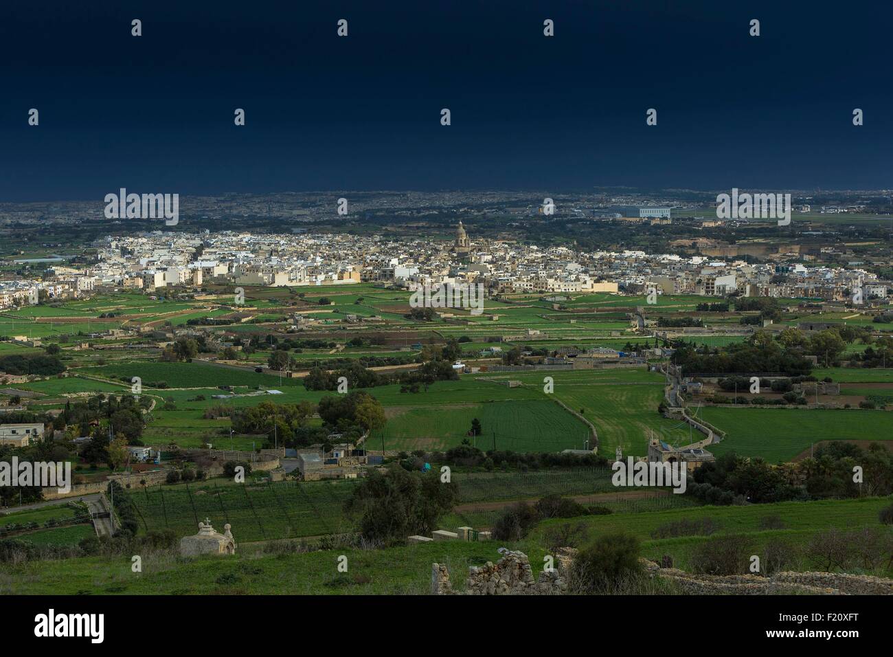 Malta, Siggiewi, la vista di un paesaggio rurale con una città in lontananza, sotto un cielo tempestoso Foto Stock