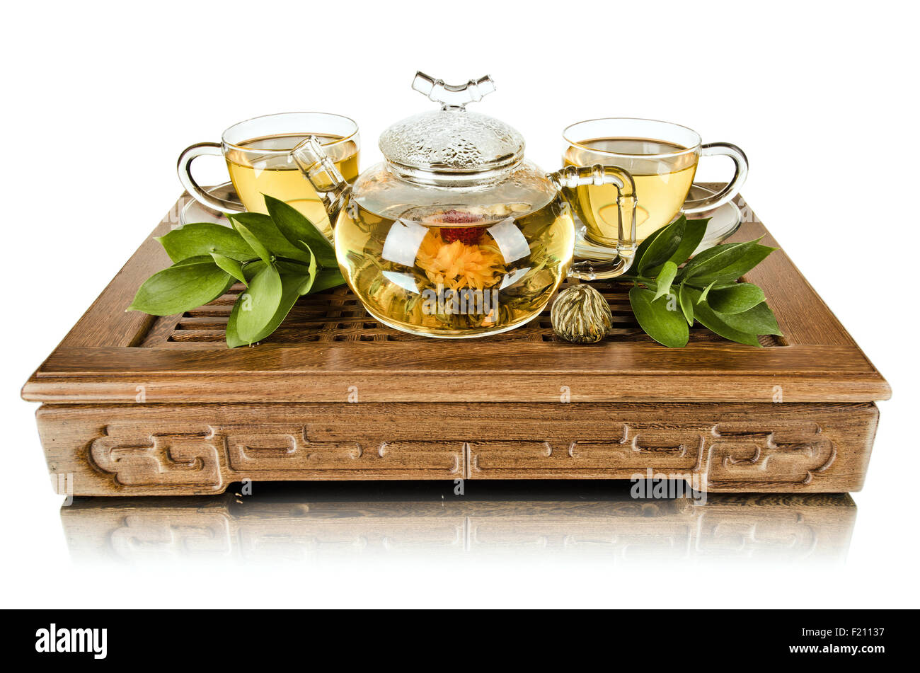 Ancora la vita del vetro teiera flusso del tè verde in coppa su legno trivet, sfondo bianco, isolata, la cerimonia del tè Foto Stock
