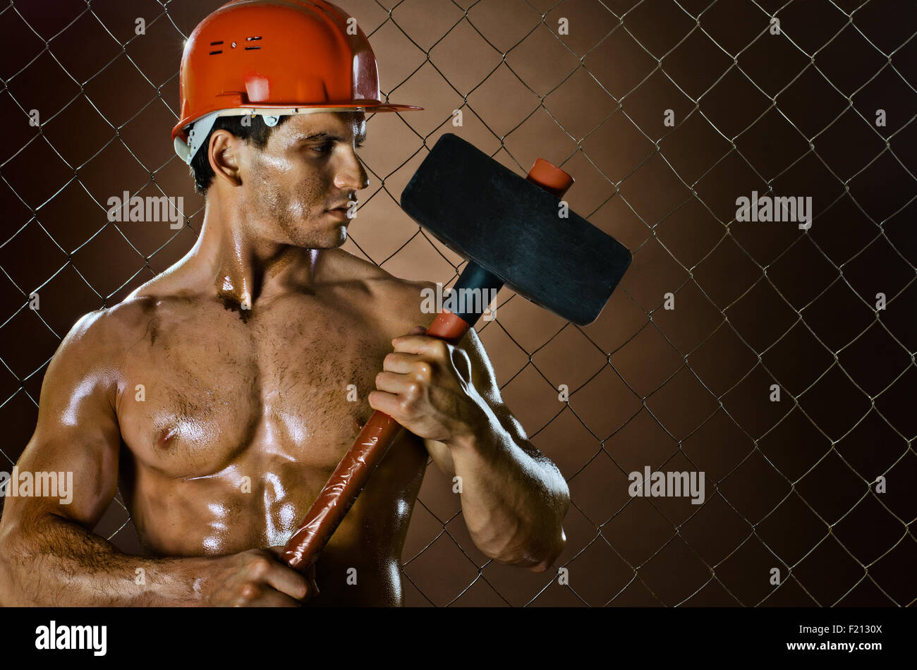 Lavoratore muscolare , nel casco di sicurezza con grande tup in mani, sulla compensazione sfondo di recinzione Foto Stock